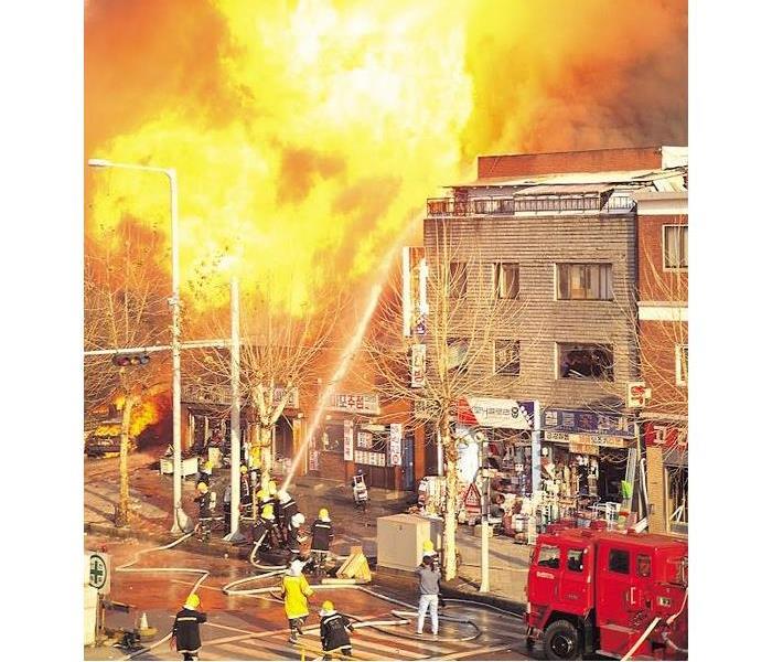 a store on fire with firemen in front of it trying to put it out with a hose